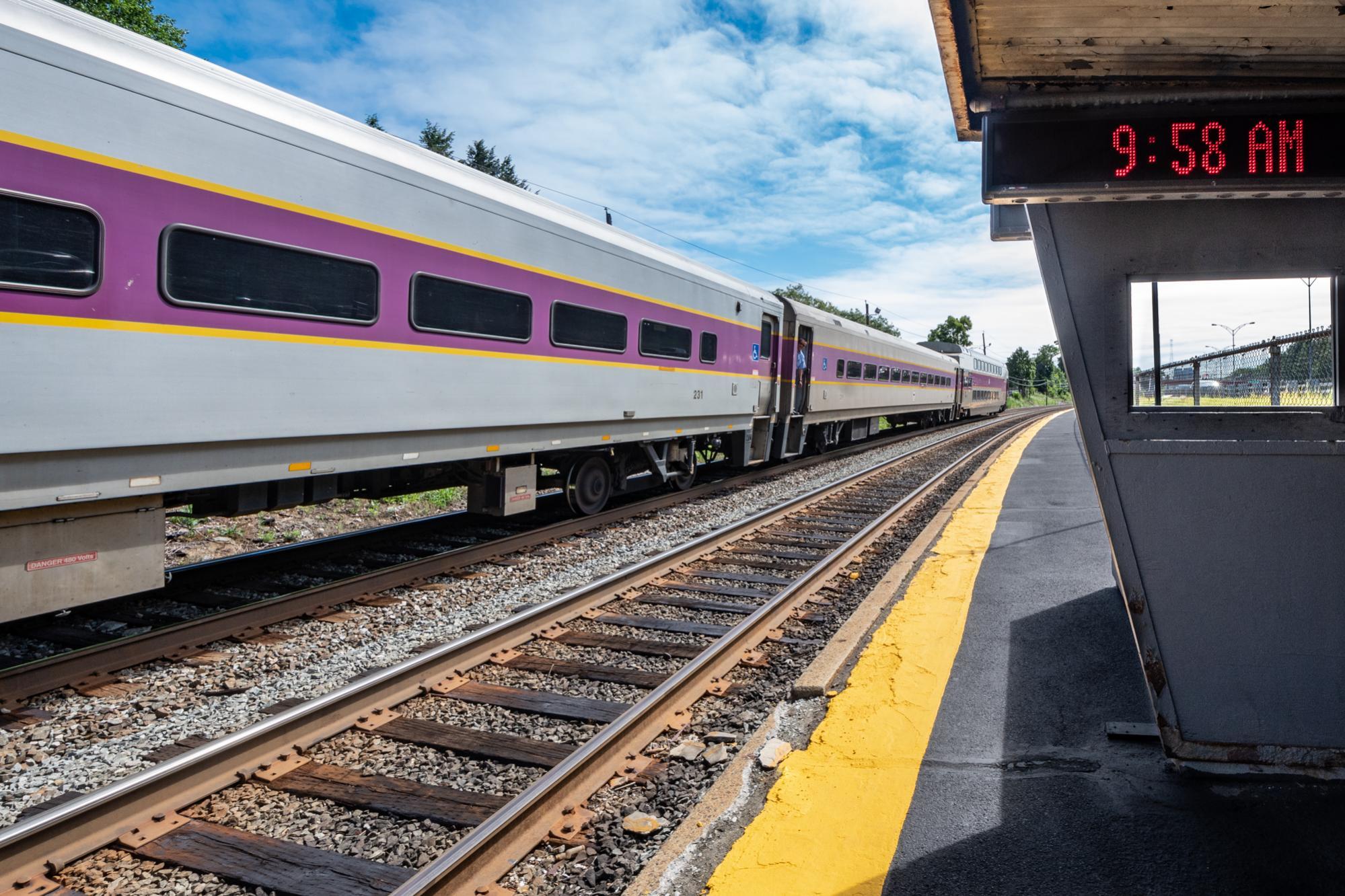 A Commter Rail train departs Auburndale station, with a coundown clock in the foreground.