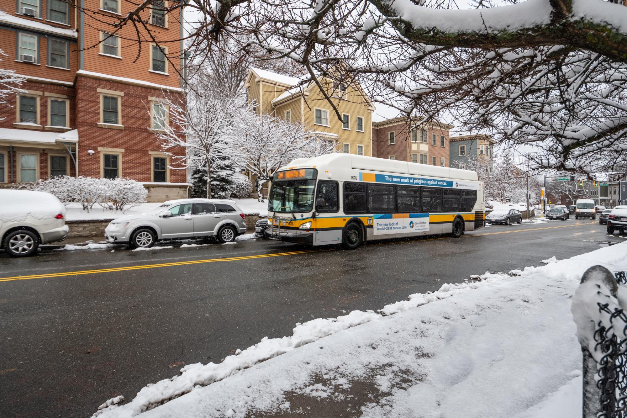 Route 39 bus travels inbound to Heath St on a cleared road, while snow is on cars and the gournd.