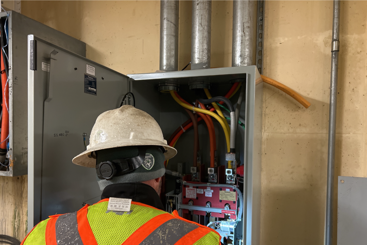 a perosn in hard hat and reflective vest looking inside a box full of wires