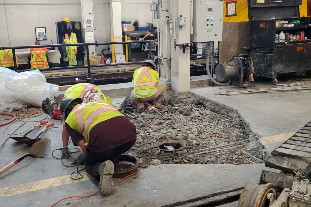 three crew members in reflective vests and hard hats working on a shallow hole in concrete flooring